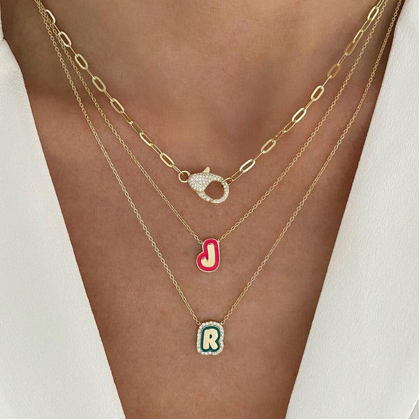 Gold necklaces with letter 'J' and 'R' pendants on a person wearing a white outfit.