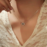 Necklace with a diamond pendant worn by a person in a lace garment.